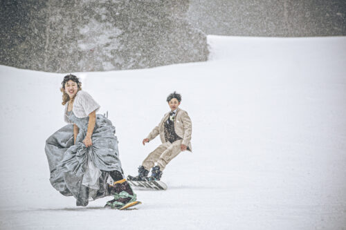 ウェディングドレスとタキシードでスノーボードを滑る新郎新婦1