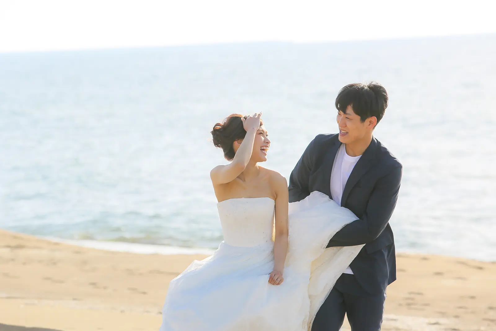 海辺でドレス姿の新婦と新郎が笑顔で撮影するフォトウェディング