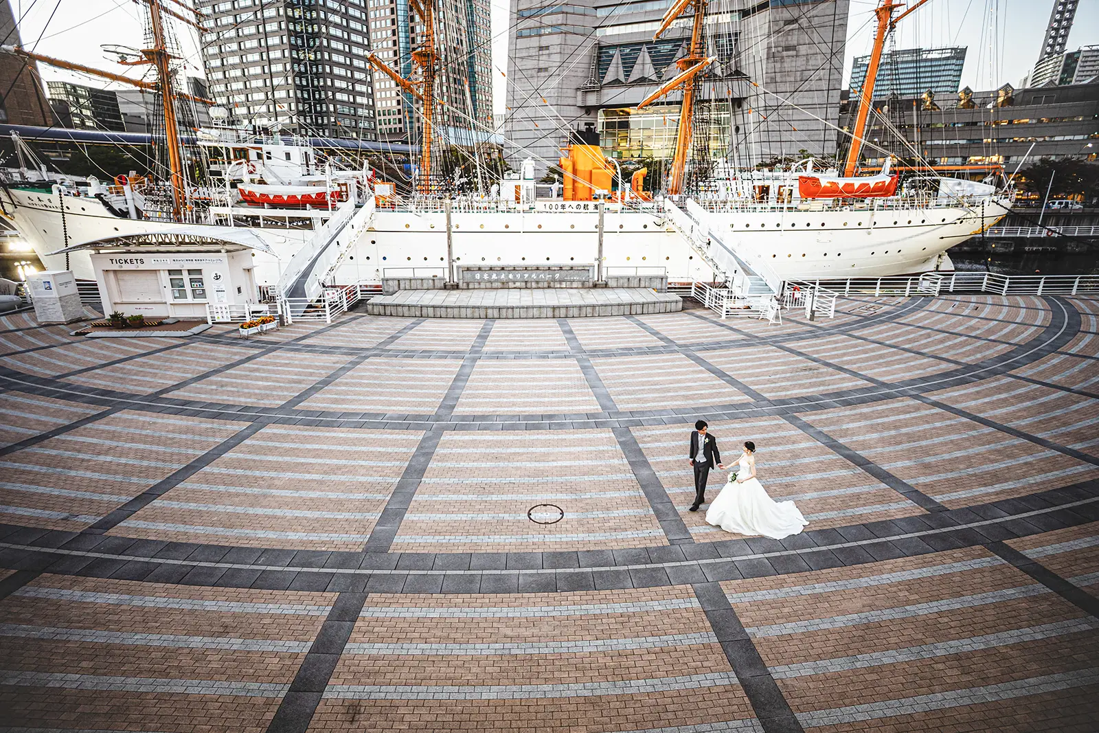 日本丸前の広い石畳空間に立つ新郎新婦を遠景で写したフォトウェディング写真