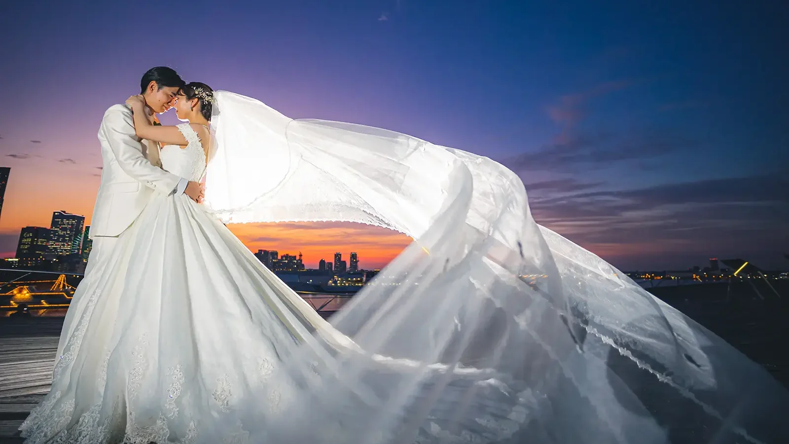 大さん橋の夕景の中でベールが大きく流れる新郎新婦のフォトウェディング写真