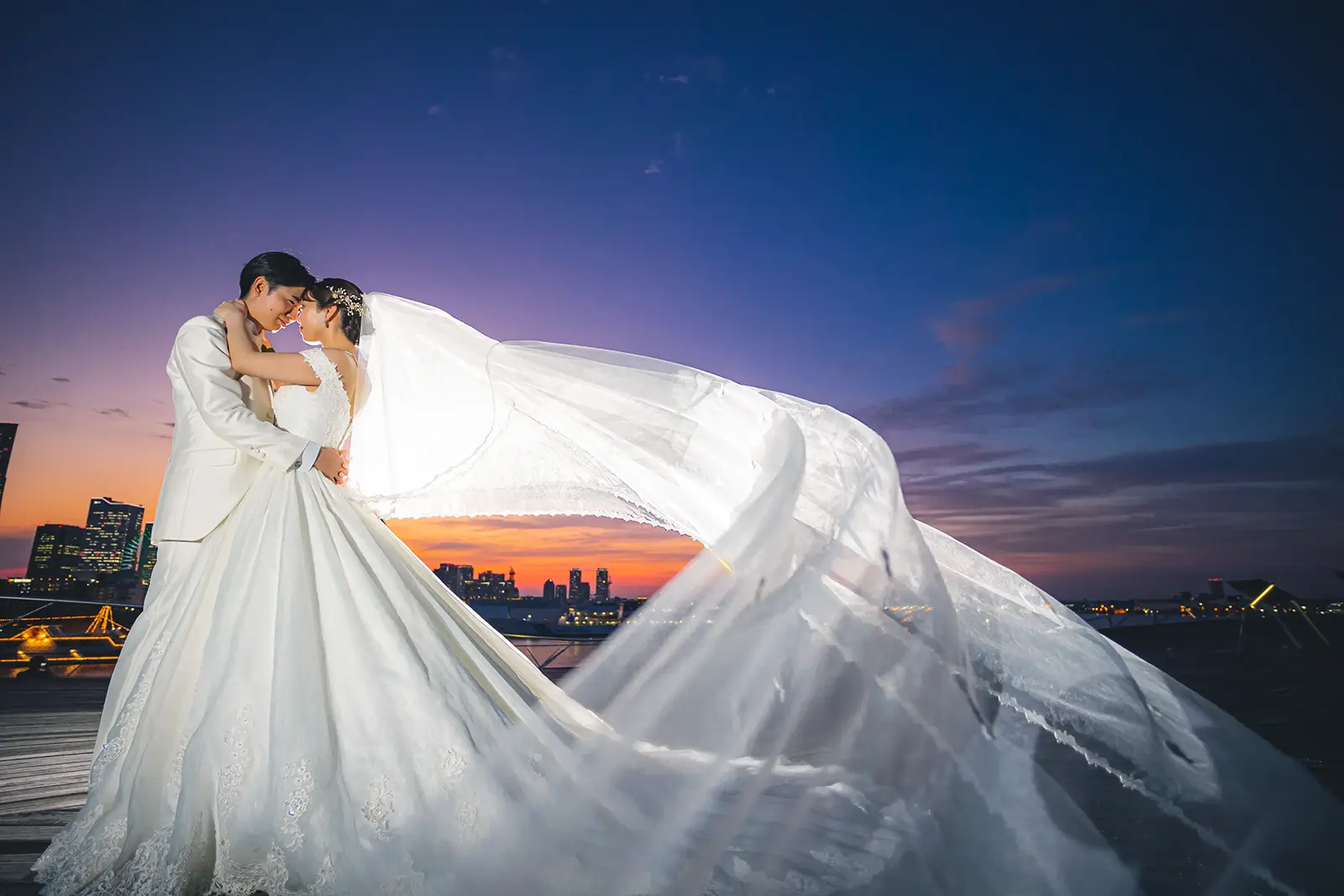 大さん橋の夕景の中でベールが大きく流れる新郎新婦のフォトウェディング写真