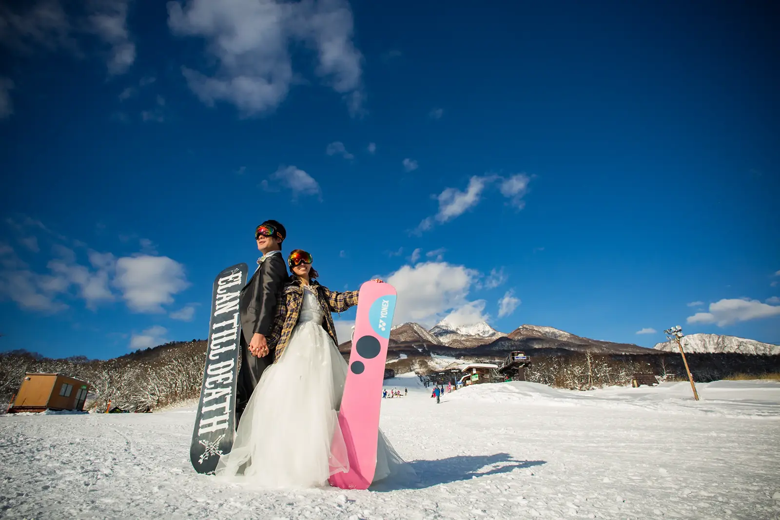雪山でスノーボードを持って並ぶ新郎新婦のウィンターフォトウェディング写真