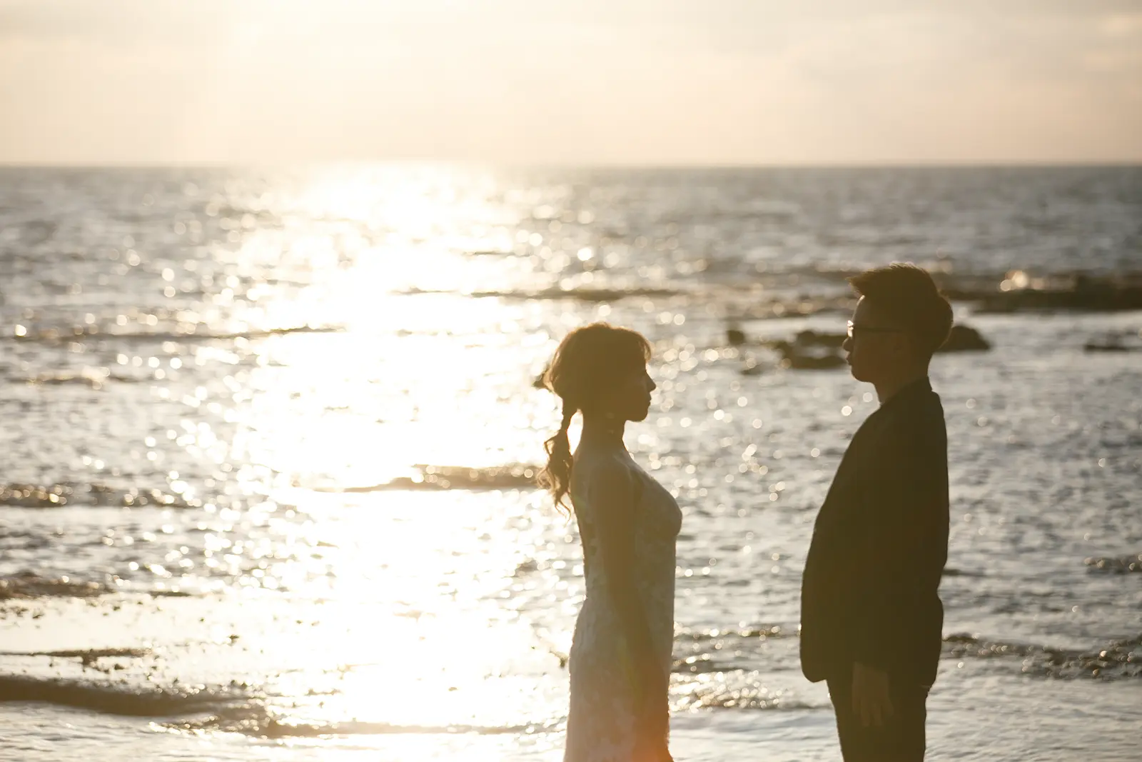 巌門の波打ち際で日本海のきらめきを背景に向かい合う新郎新婦