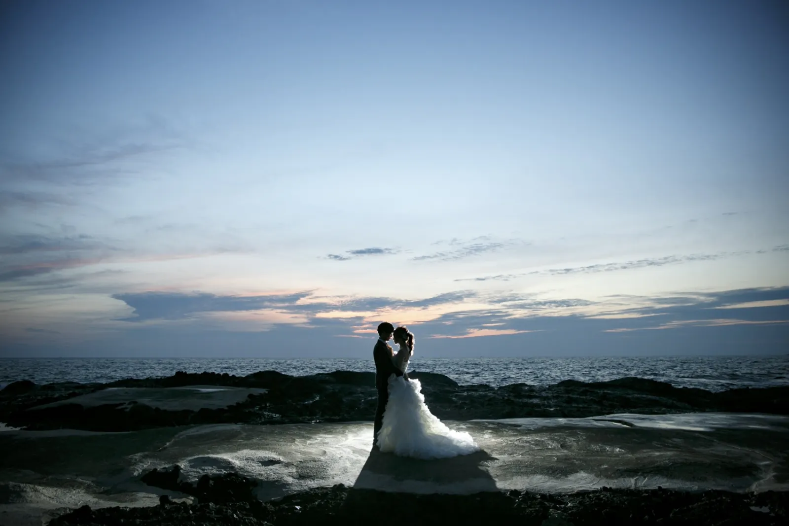 巌門の夕暮れの海を背景に寄り添う新郎新婦のシルエット