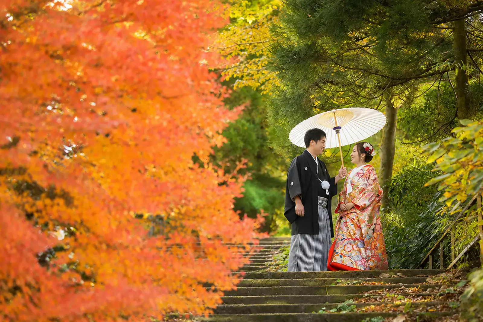 紅葉を背景に番傘を持つ和装の新郎新婦