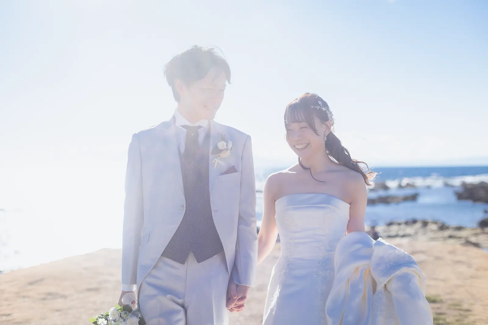 風のある一色海岸で自然な笑顔を見せる新郎新婦