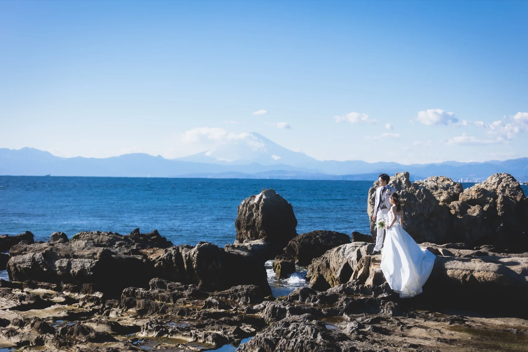 小磯の鼻の岩場に立ち富士山と海を背景にした新郎新婦、葉山の洋装フォトウェディング