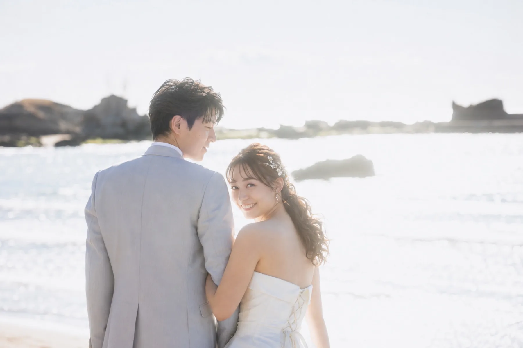 冬の葉山の海辺で笑顔で振り返る新婦と新郎、自然体の洋装フォトウェディング