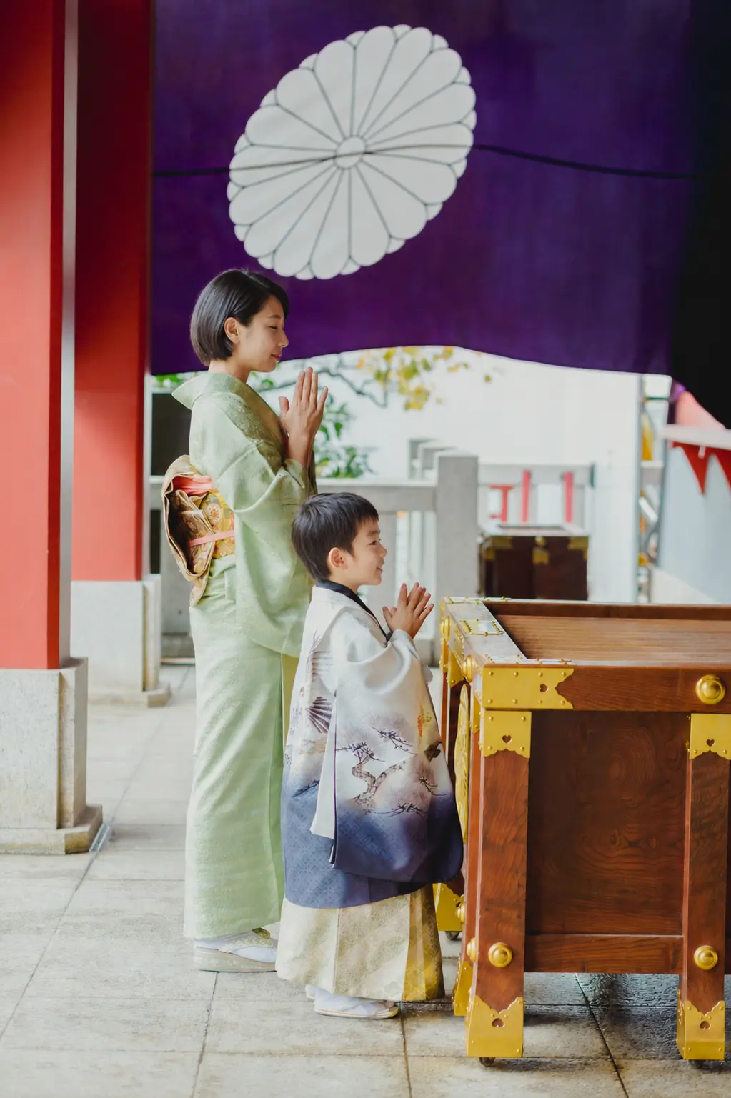 紫の幕が下がる日枝神社の拝殿前で手を合わせる羽織袴姿の5歳の男の子と母、七五三出張撮影（東京）