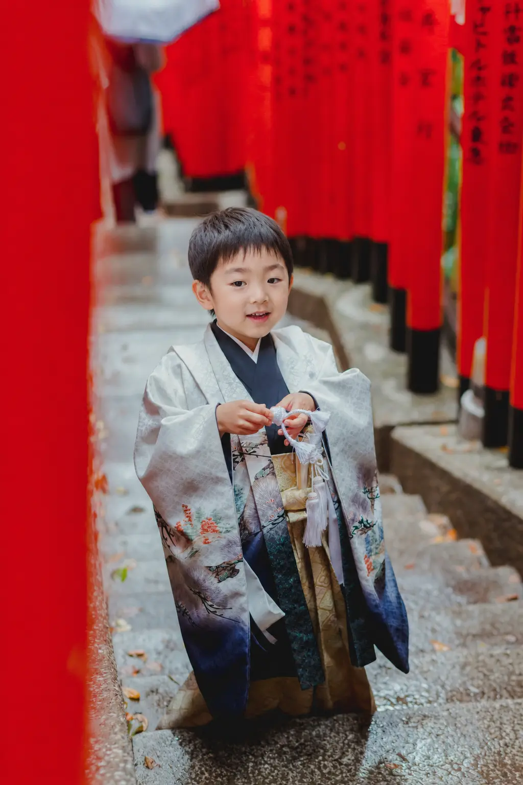 朱い鳥居が続く石段で白い羽織紐の房を指先でさわる5歳の男の子、日枝神社の七五三出張撮影（東京）
