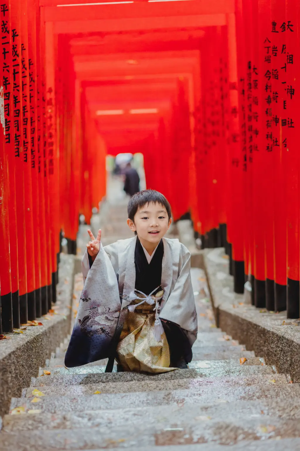 朱い鳥居のトンネルの石段でしゃがんでピースをする羽織袴姿の5歳の男の子、七五三出張撮影（東京・日枝神社）