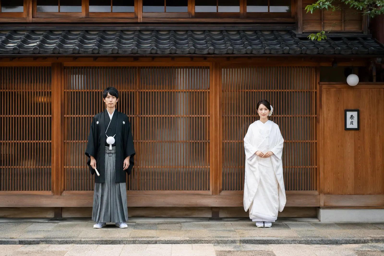 ひがし茶屋街の格子戸を背景に白無垢の新婦と紋付袴の新郎が立つ和装前撮り写真
