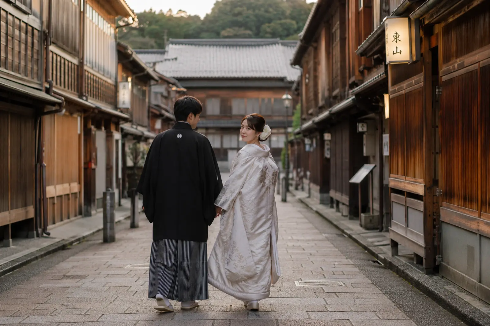 金沢ひがし茶屋街の町並みを白無垢の新婦と紋付袴の新郎が手をつないで歩く後ろ姿の写真