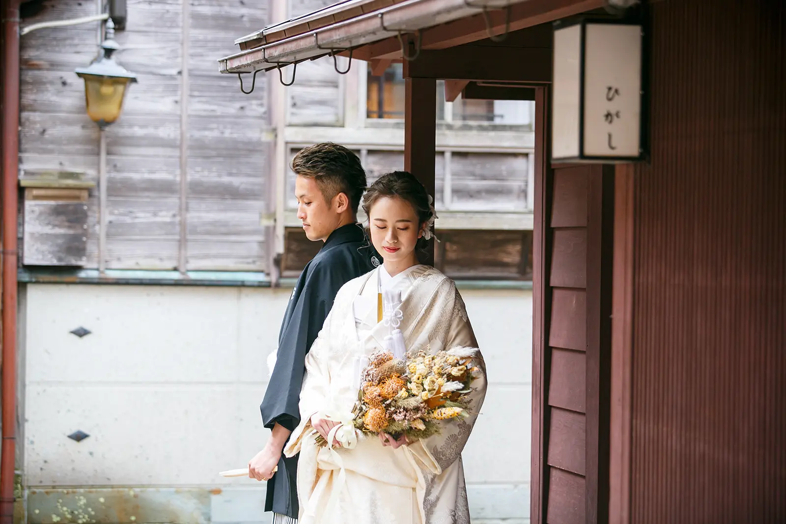 金沢のひがし茶屋街の町家前でブーケを持つ白無垢姿の新婦と紋付袴の新郎