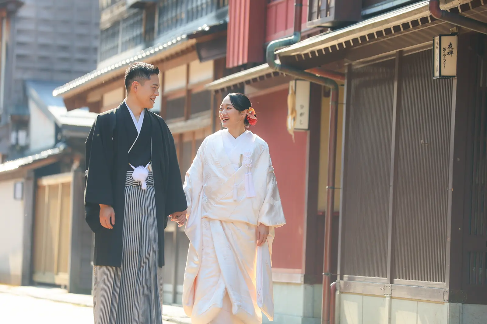 金沢のひがし茶屋街で町家の前を手をつないで歩く白無垢姿の新婦と紋付袴の新郎