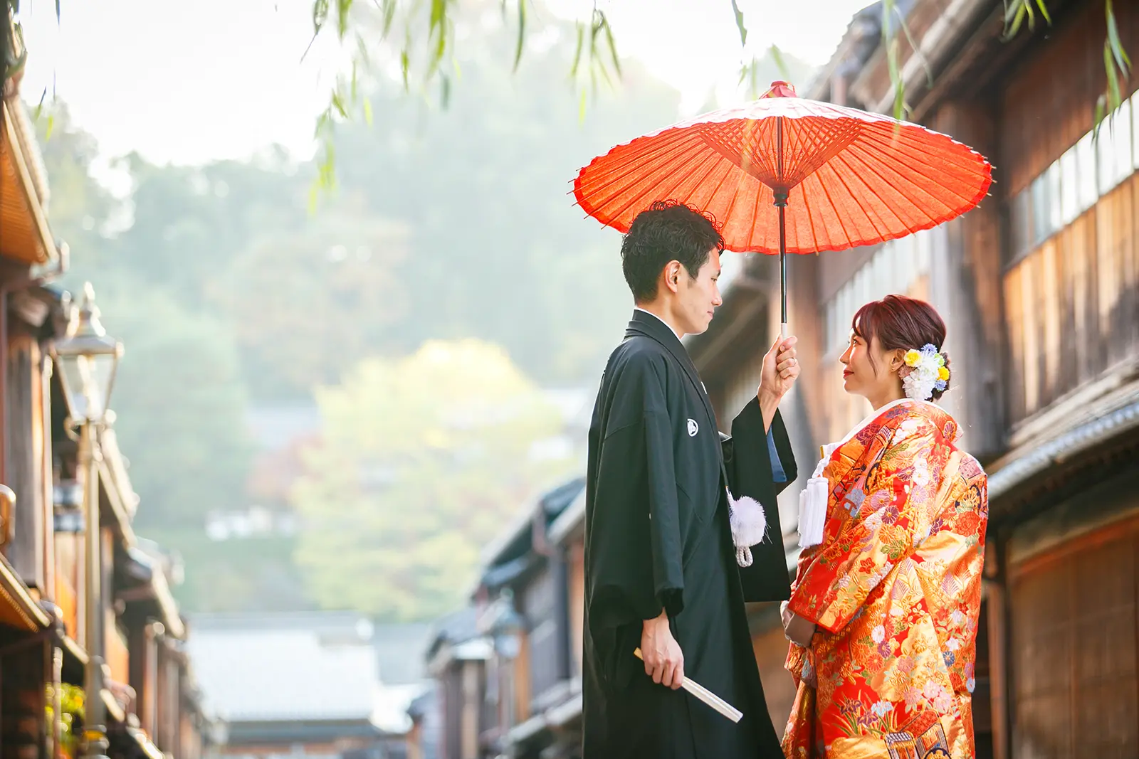 金沢のひがし茶屋街で赤い和傘の下に立つ和装姿の新郎新婦