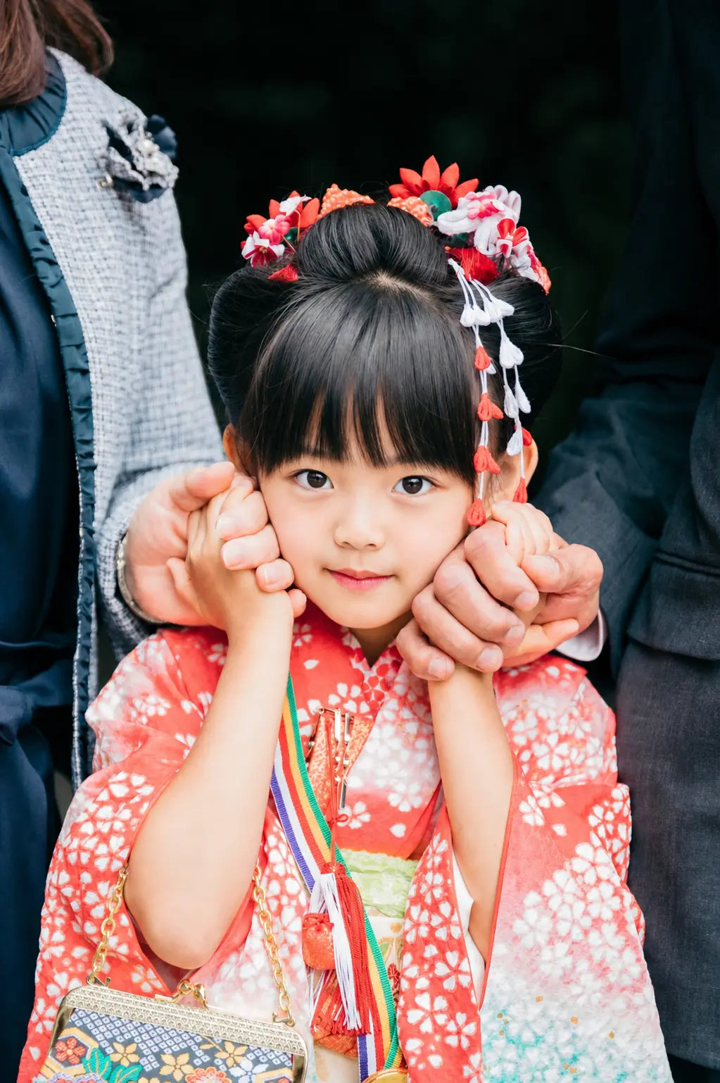 両方の頬に家族の手が添えられて笑う7歳の女の子、四つ身の七五三（本牧神社・横浜）