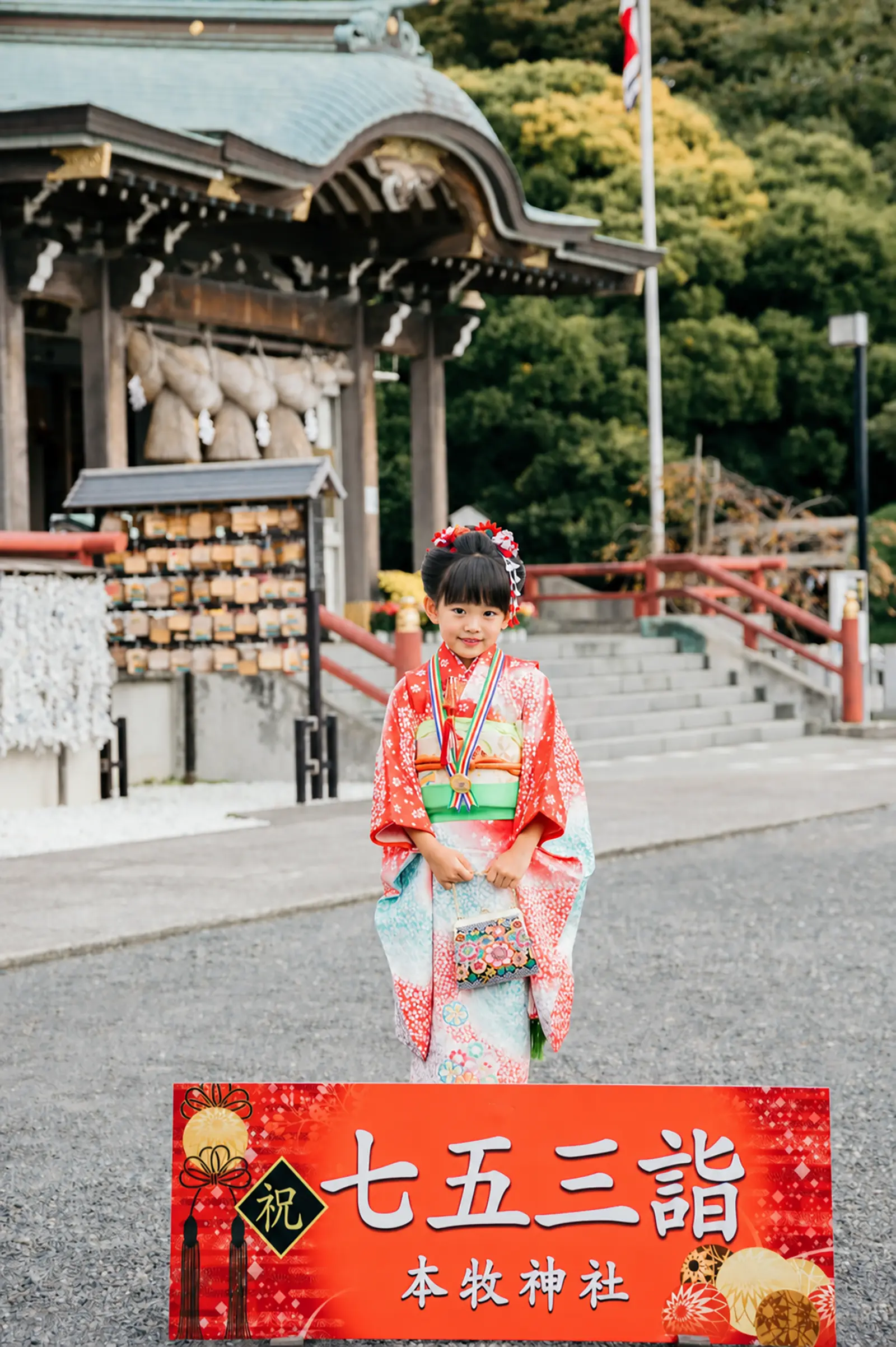 本牧神社の祝七五三詣の看板の前に立つ7歳の女の子、四つ身とがま口バッグの七五三（横浜市中区）