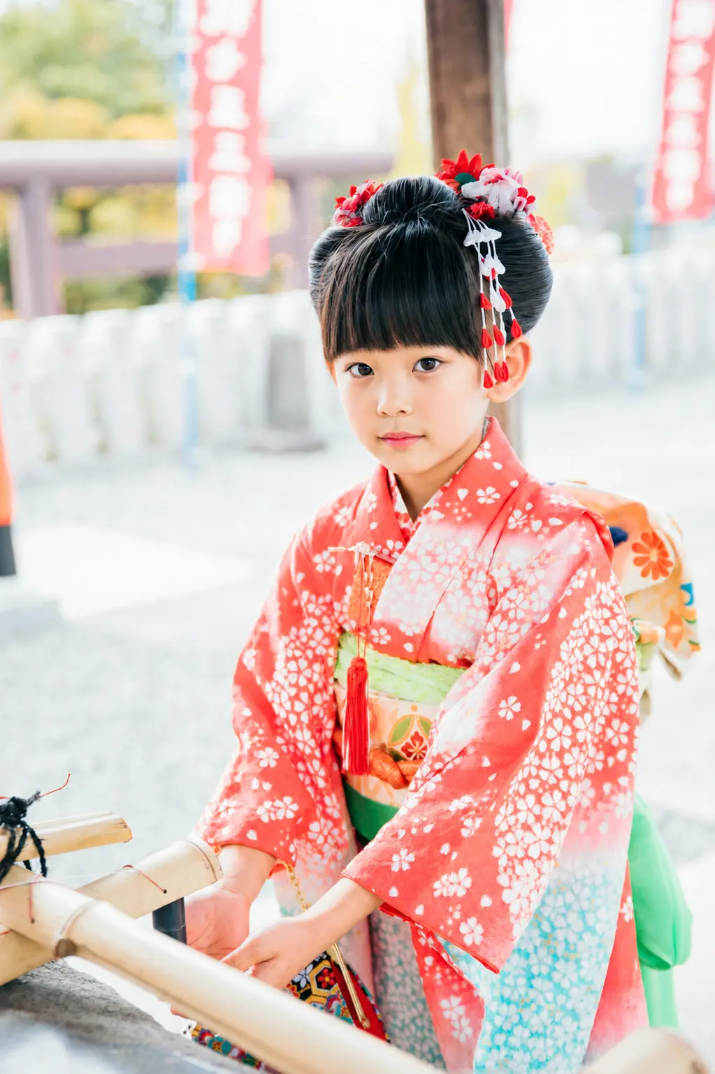 本牧神社の手水舎の前でこちらを向く7歳の女の子、朱赤の四つ身と日本髪の七五三