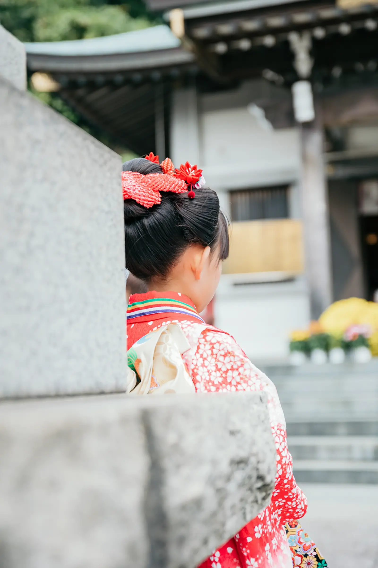 本牧神社の石柱のかげに立つ7歳の女の子の後ろ姿、日本髪と朱赤の四つ身の七五三（横浜）