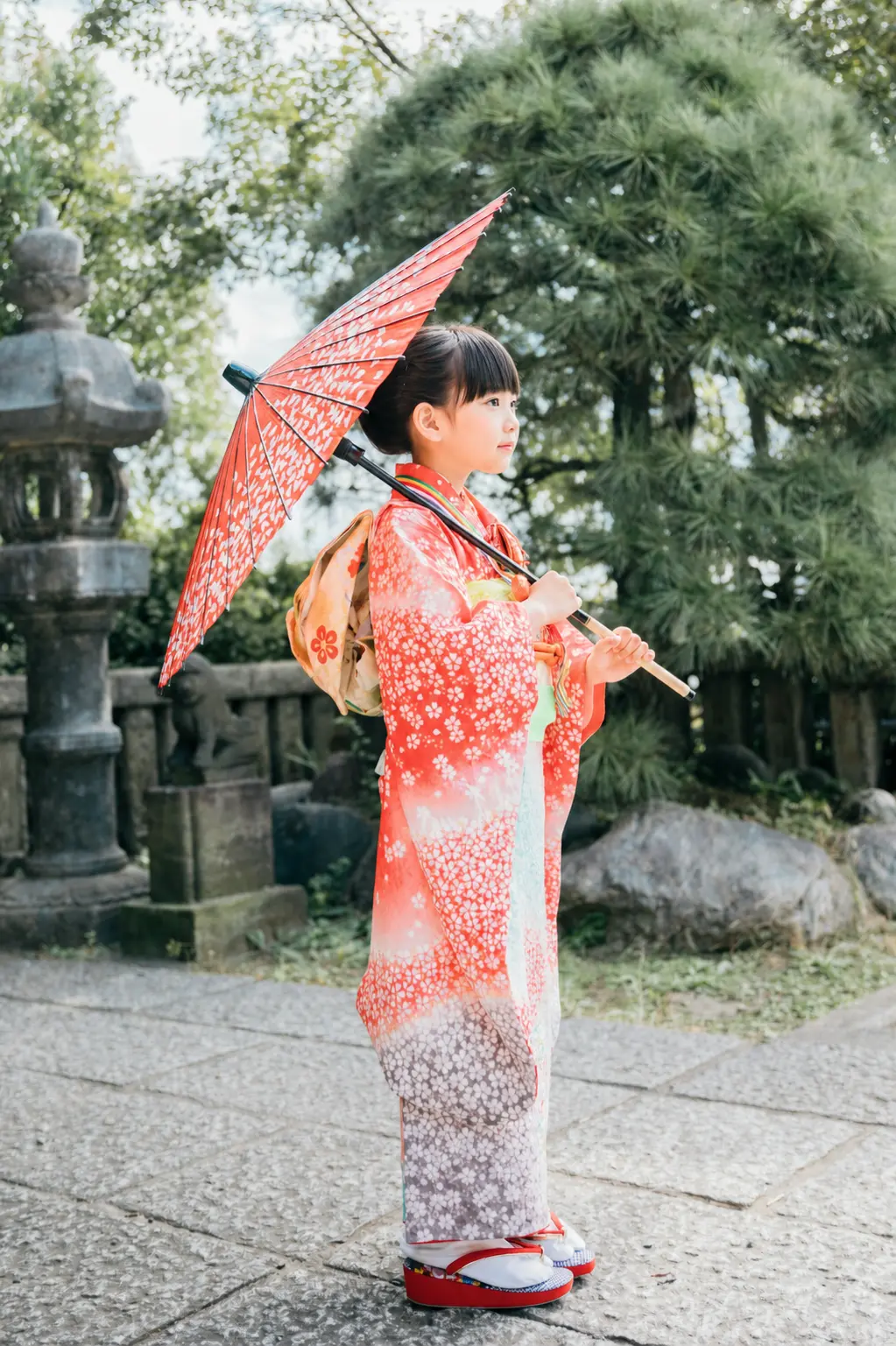 本牧神社の石灯籠のそばで赤い和傘を持って立つ7歳の女の子、四つ身の七五三（横浜）