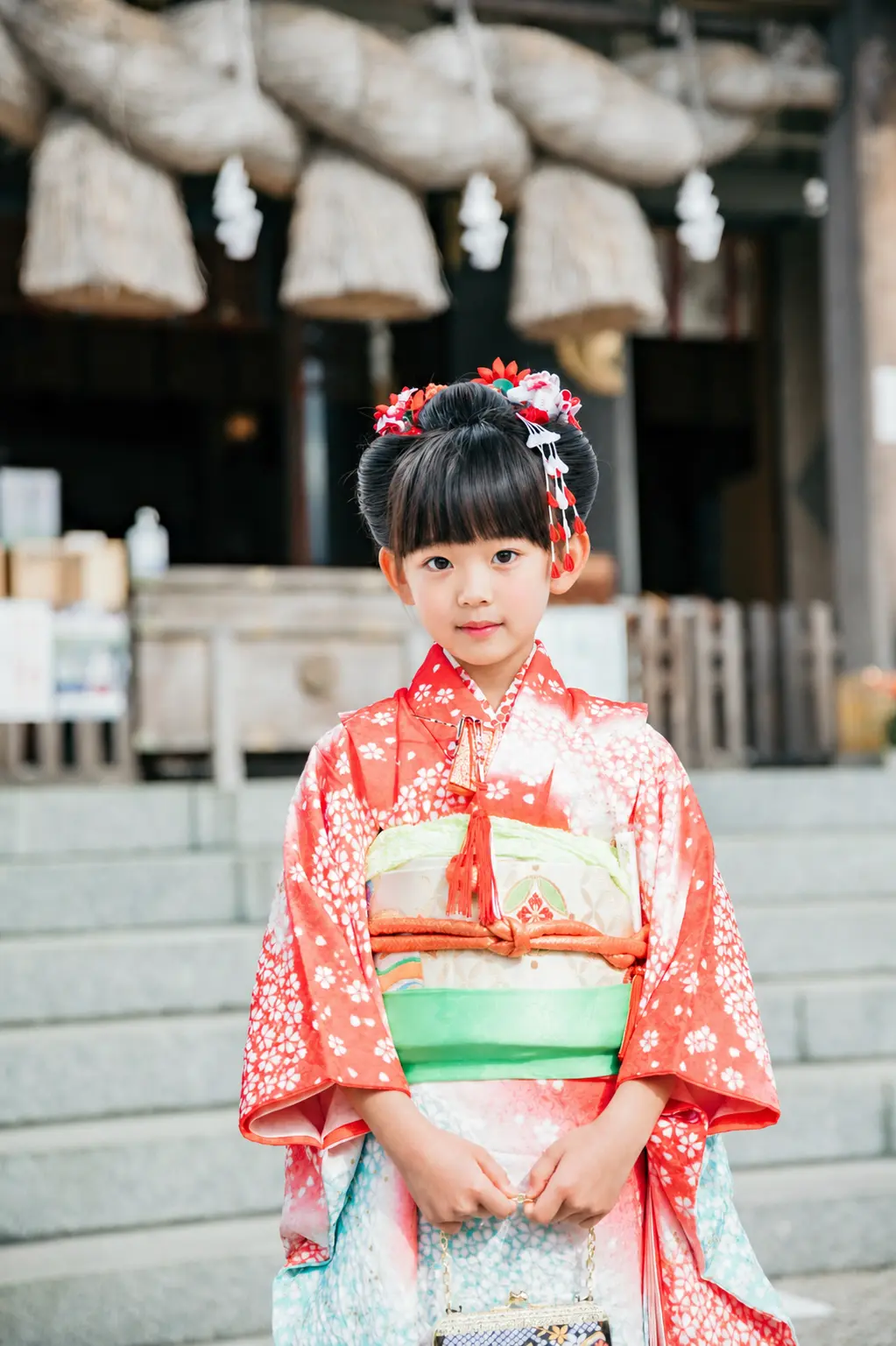 本牧神社の拝殿に下がる大注連縄を背に立つ7歳の女の子、朱赤の四つ身と日本髪の七五三（横浜市中区）