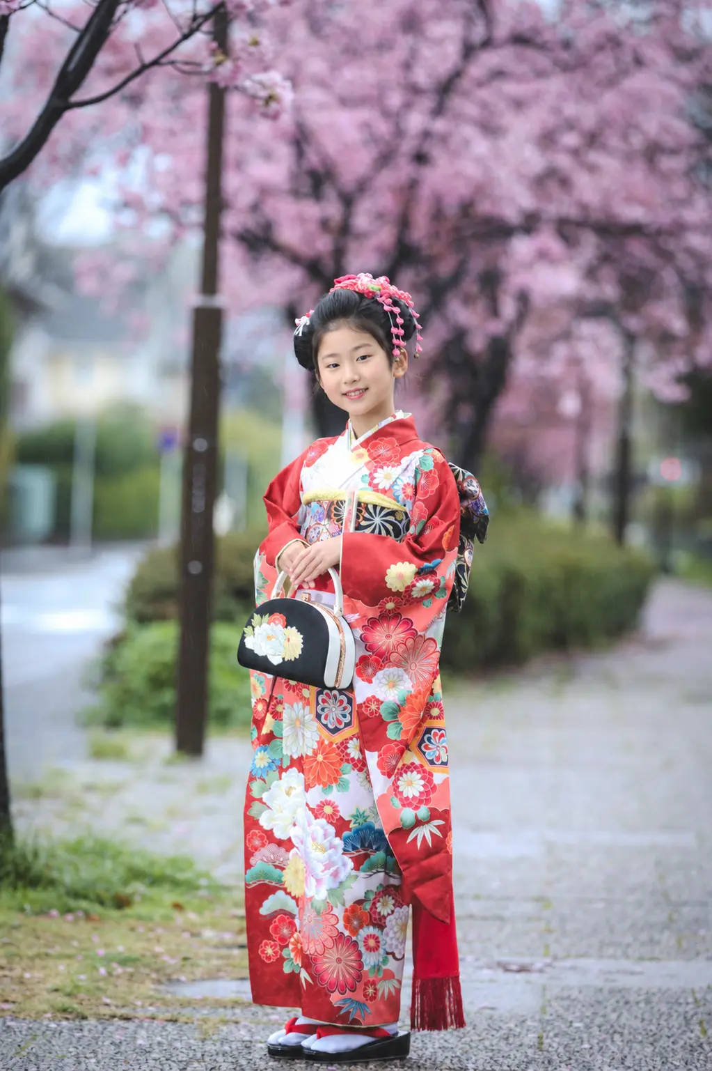 満開の桜並木に立つ7歳の女の子、赤い四つ身姿の七五三出張撮影（本牧神社・横浜）