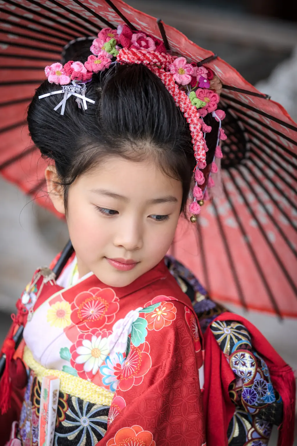 赤い和傘の下でまなざしを伏せる7歳の女の子、四つ身と花かんざしの七五三（本牧神社・横浜）
