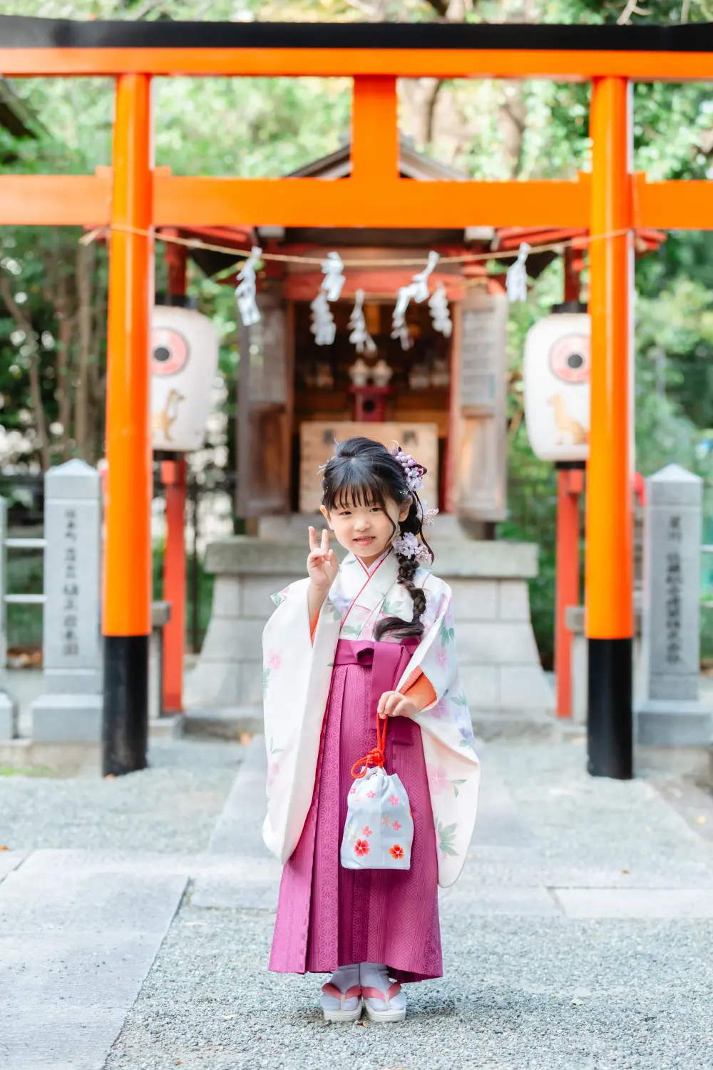 朱い鳥居と白い提灯を背に、ピースサインをする袴すがたの7歳の女の子。星川杉山神社の七五三（横浜市保土ケ谷区）