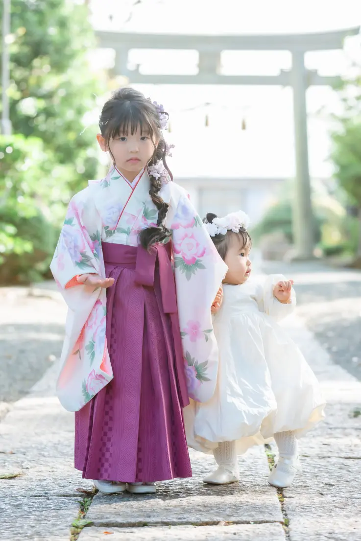 逆光の石鳥居を背に、妹と並んで立つ袴すがたの7歳の女の子。星川杉山神社の七五三きょうだい撮影（横浜）