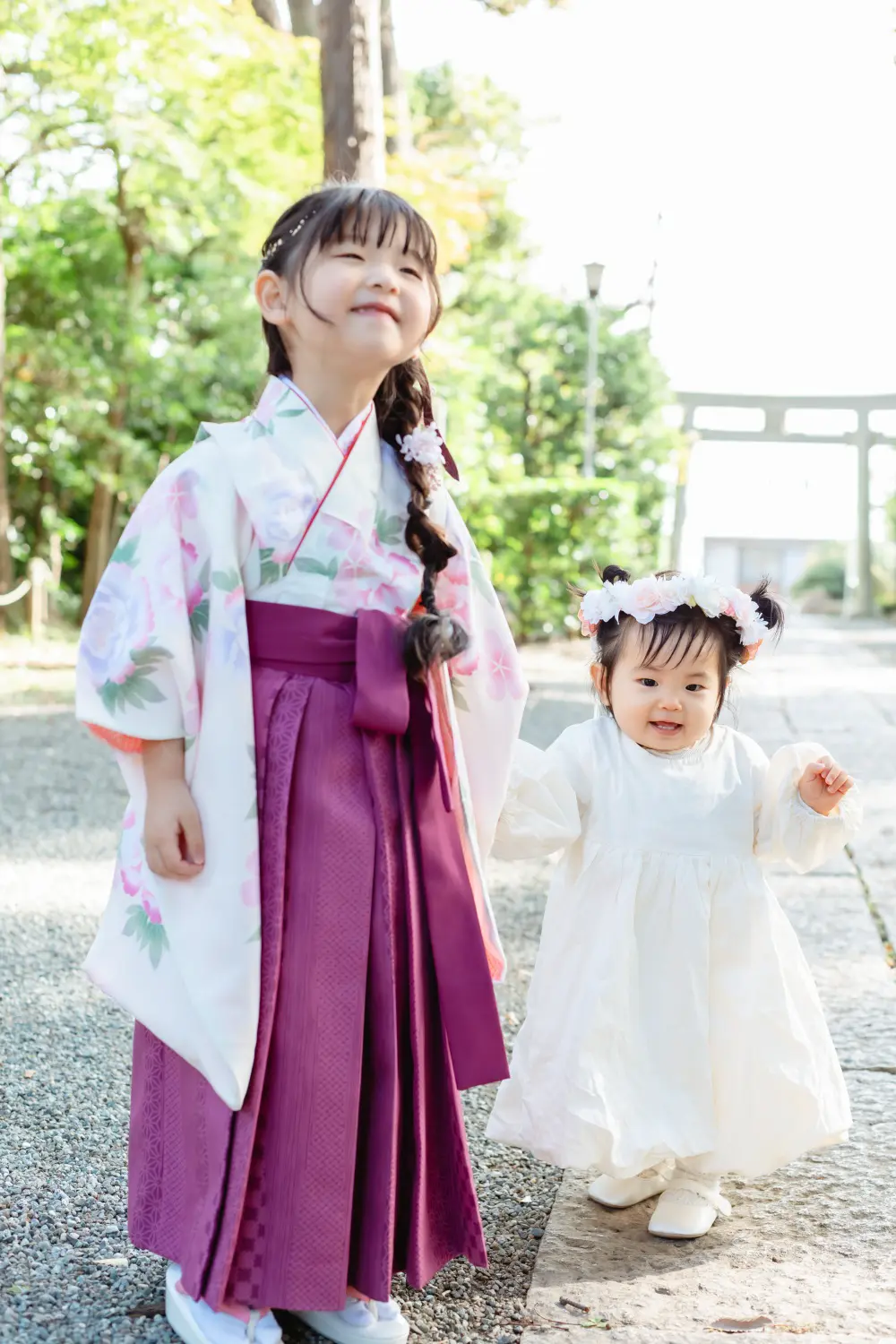 白いワンピースに花冠の妹と手をつなぎ、目を細めて笑う袴すがたの7歳の女の子。星川杉山神社の七五三出張撮影（横浜）