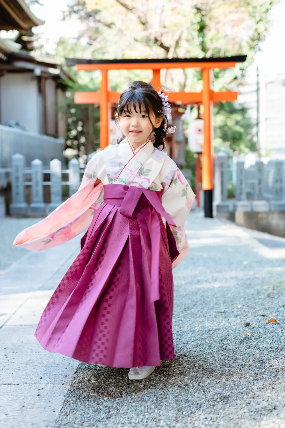 参道を歩きながら着物の袖を翻す、袴すがたの7歳の女の子。朱い鳥居を背にした星川杉山神社の七五三出張撮影（横浜）