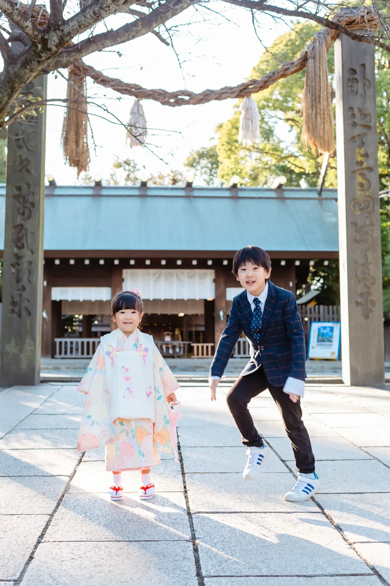お兄ちゃんが大きくジャンプする横で正面を向いて笑う3歳の女の子、七五三の被布姿（伊勢山皇大神宮・横浜）