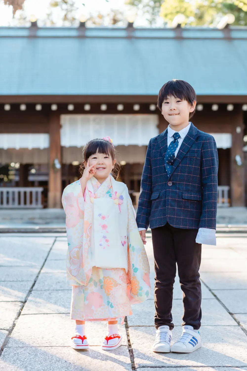 拝殿前でお兄ちゃんと手をつなぎピースをする3歳の女の子、七五三の被布姿（伊勢山皇大神宮・横浜）