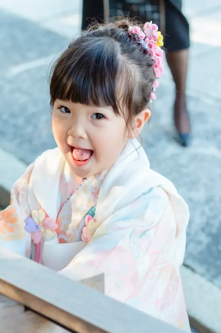 手水舎から見上げて舌を出す3歳の女の子、七五三の着物姿（伊勢山皇大神宮・横浜）