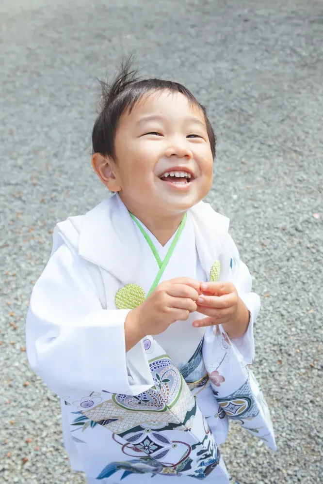 玉砂利を背に見上げて大きく笑う3歳の男の子、白い被布姿の七五三（伊勢山皇大神宮・横浜）