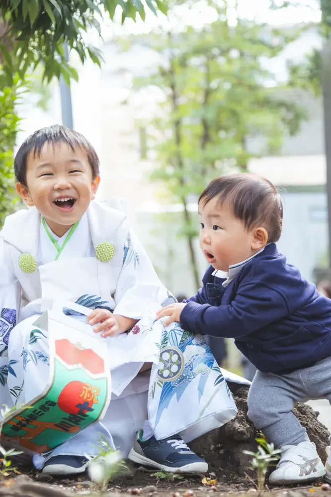 土の段差に並んで大笑いする白い被布姿の3歳の男の子と年下の男の子、七五三（伊勢山皇大神宮・横浜）