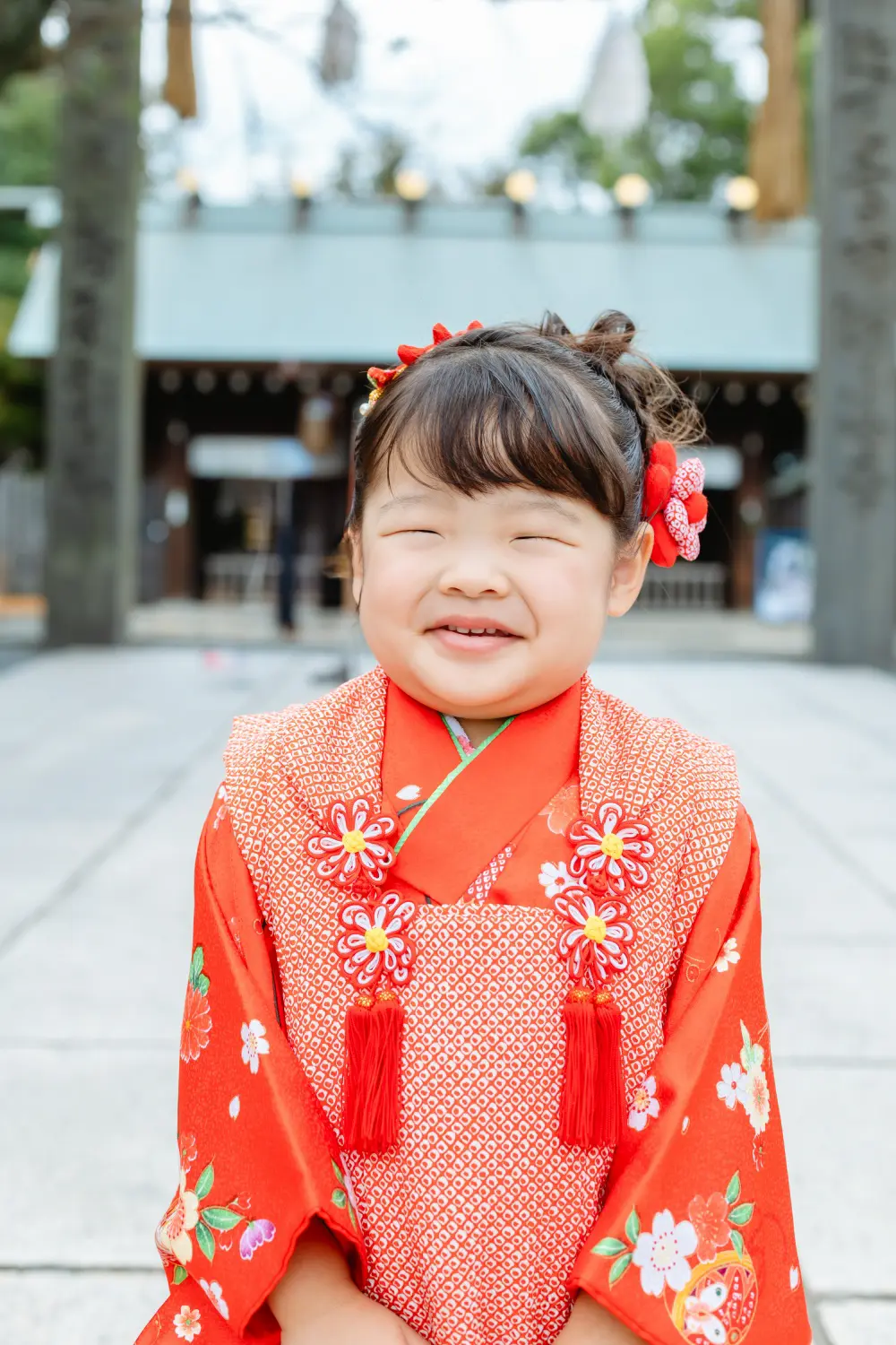 目を閉じて歯を見せて笑う赤い被布姿の3歳の女の子、七五三（伊勢山皇大神宮・横浜）