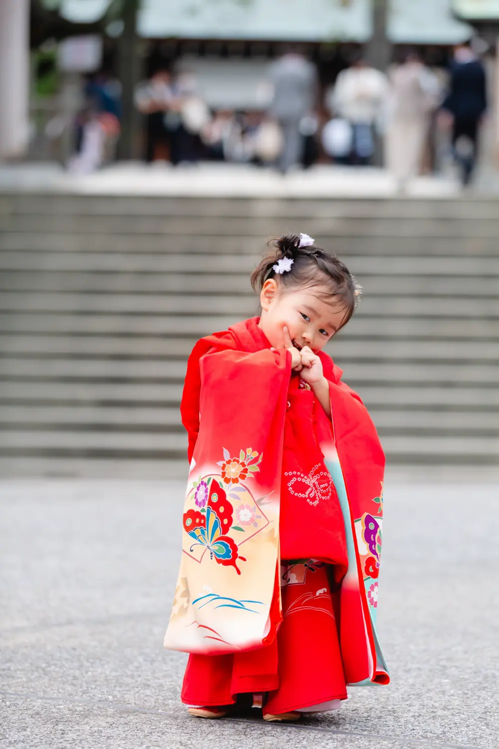 身をよじってはにかむ朱赤の被布姿の3歳の女の子、七五三前撮り（伊勢山皇大神宮・横浜）