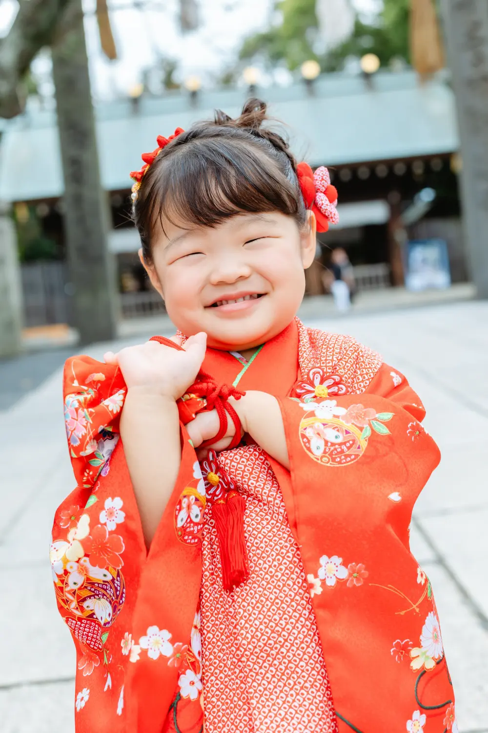 手を胸元で合わせて目を細めて笑う、赤い被布姿の3歳の女の子（七五三・伊勢山皇大神宮）