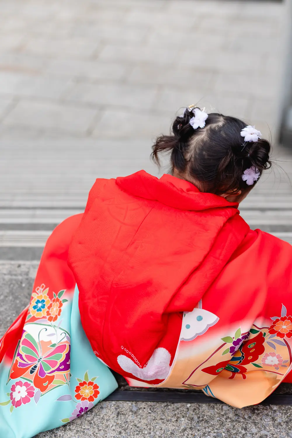 石段に腰かけた3歳の女の子を斜め後ろから見たお団子ヘアと被布の背中、七五三（伊勢山皇大神宮・横浜）
