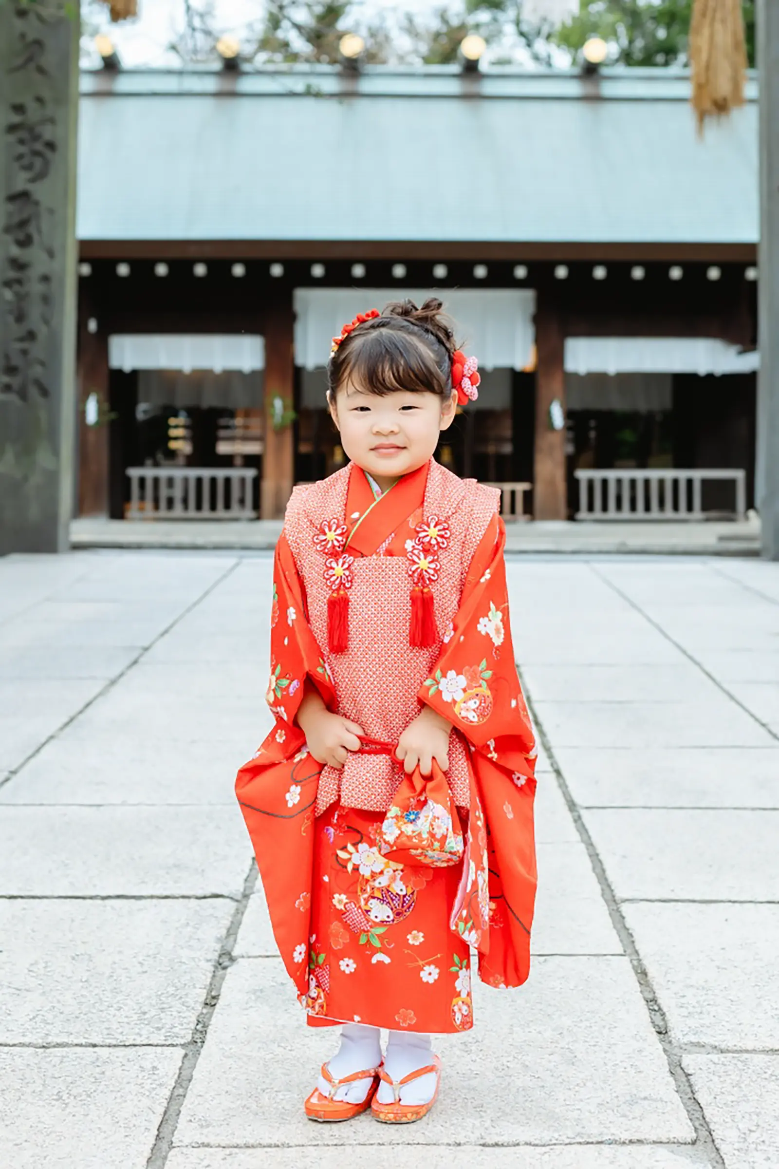 伊勢山皇大神宮の社殿を背に立つ、赤い被布姿の3歳の女の子の七五三全身写真（横浜）