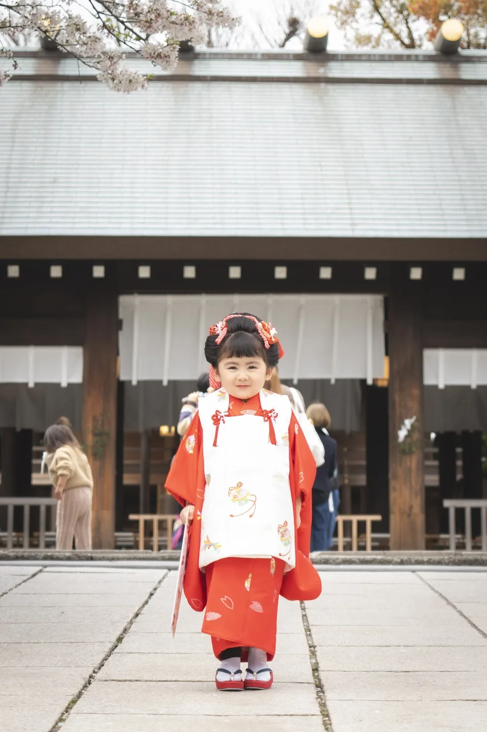 伊勢山皇大神宮の社殿前に立つ3歳の女の子、赤い被布姿の七五三出張撮影（横浜）