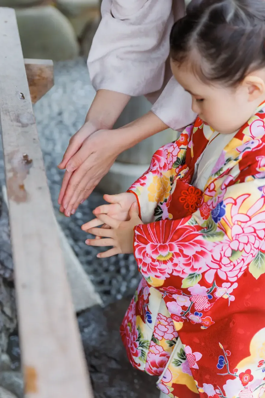 手水舎で母に手を添えられて手を清める3歳の女の子、赤い被布姿（伊勢山皇大神宮・横浜の七五三）