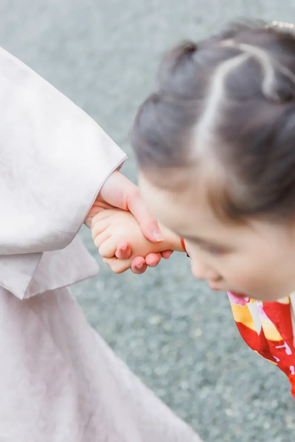 母と手をつないだ小さな手にピントを置いた縦位置、赤い被布姿の3歳の女の子（伊勢山皇大神宮・横浜の七五三）
