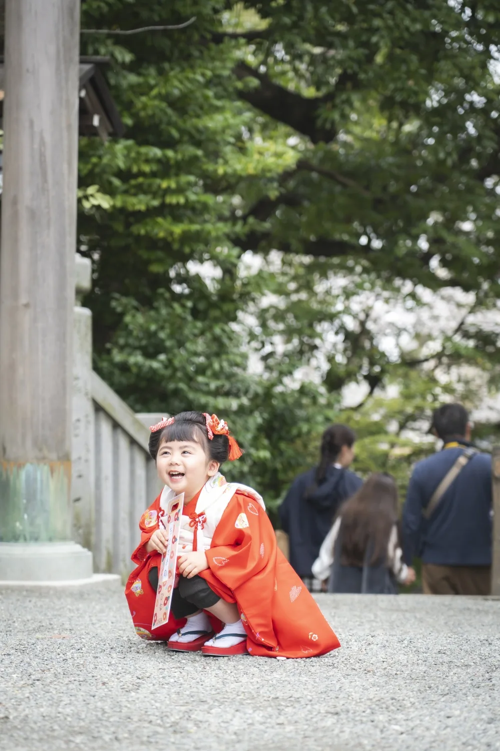 石鳥居のそばでしゃがんで笑う3歳の女の子、被布姿（伊勢山皇大神宮・七五三）