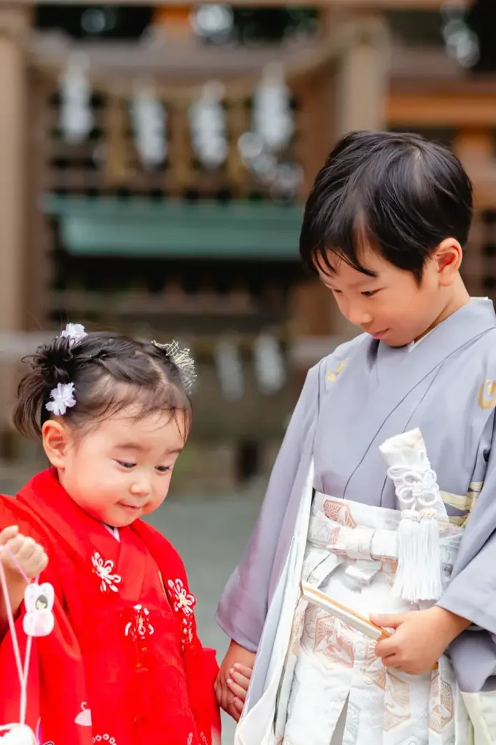 手をつないだまま小さな巾着をのぞき込む兄妹、七五三の被布と羽織袴（伊勢山皇大神宮・横浜）