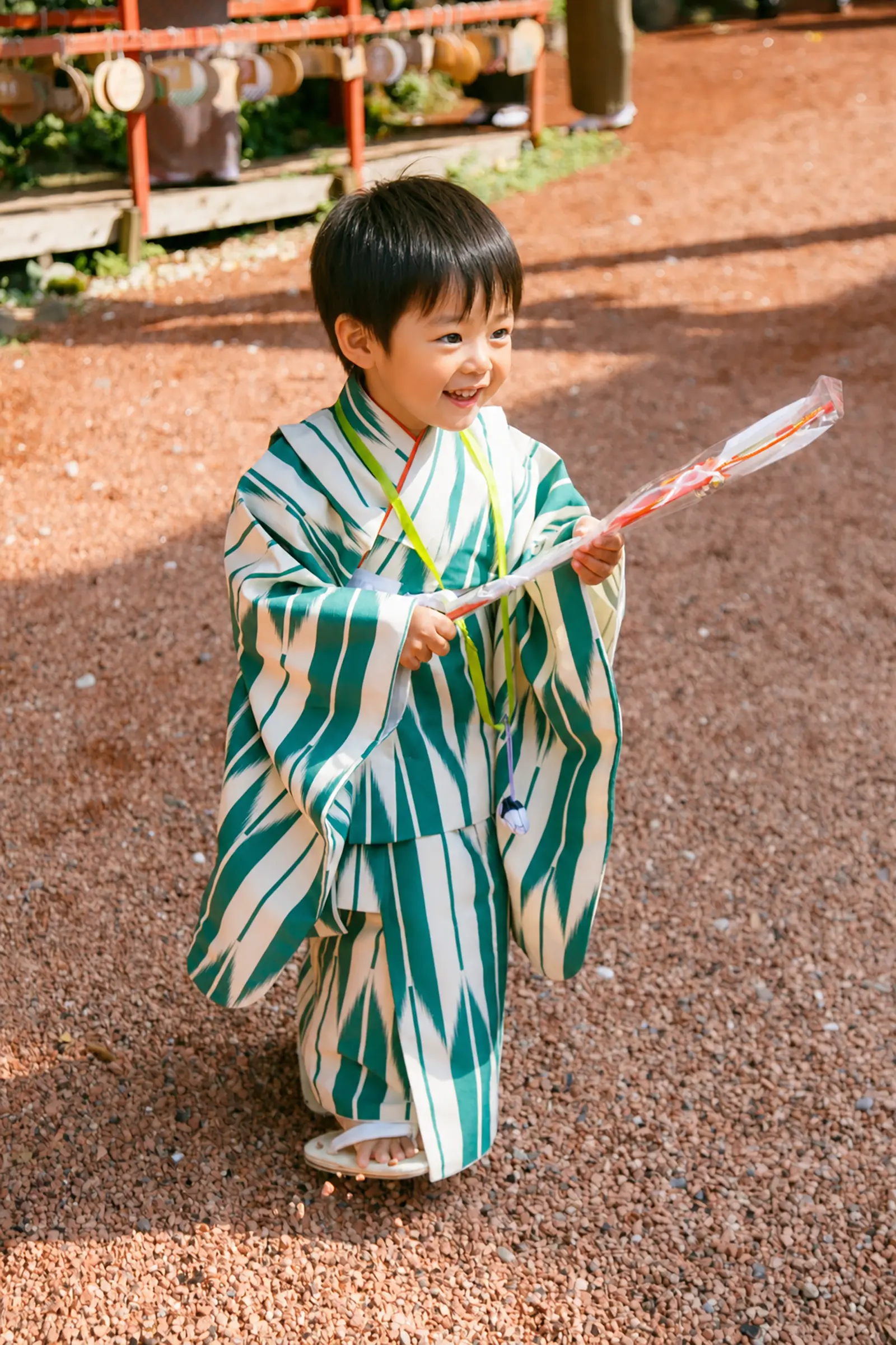 授与品の袋を両手に持ち玉砂利の上を歩く3歳の男の子｜石浦神社の七五三出張撮影（金沢）