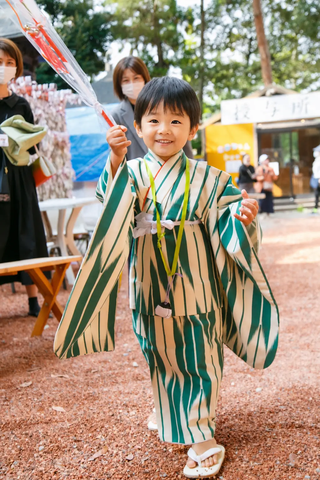 授与所の前で袋を高く掲げて歩く3歳の男の子、深緑と生成りの着物｜石浦神社の七五三出張撮影（金沢）