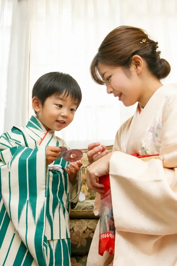 訪問着姿の母と向かい合い手元のものを見せる3歳の男の子、深緑の着物｜石浦神社の七五三出張撮影（金沢）
